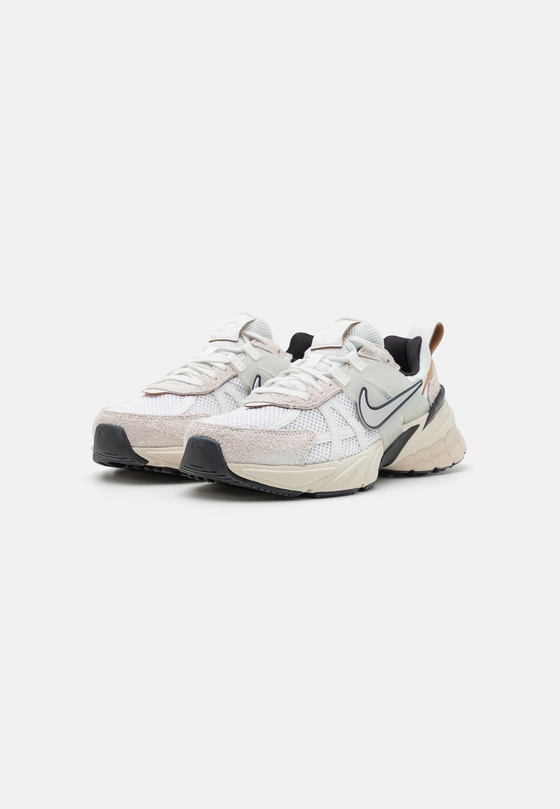Zapatillas de malla blanca y ante con acentos negros, puntera redondeada, cuello acolchado y suela de goma texturizada. Logo de Nike en gris en el lateral.