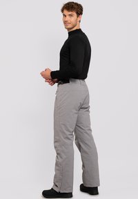 Grijze geïsoleerde broek met een textuurstof, voorzien van een recht gesneden ontwerp en een zwarte tailleband. Gecombineerd met een zwart lang innovatieve shirt.