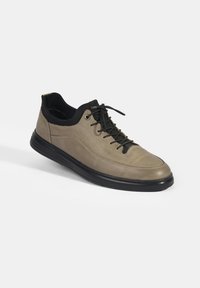 Chaussure pour homme à lacets en cuir beige avec des accents noirs, texture lisse, bout rond et semelle en caoutchouc noir pour l'adhérence.
