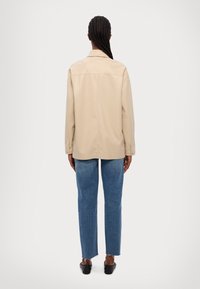 Beige, langwerpige shirt met lange mouwen en een ontspannen pasvorm, zachte textuur en een rechte zoom, gecombineerd met lichtblauwe, hoge taille jeans met uiteinden die rafelen.