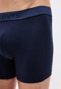 Κοντινό ενός ατόμου που φοράει μπλε ναυτικό μπόξερ με αντίστοιχη μέση που έχει διακριτικό κείμενο λογότυπου.