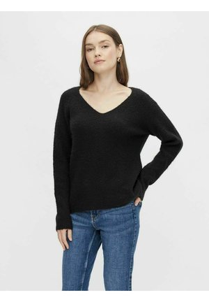 Schwarzer Strickpullover mit V-Ausschnitt und langen Ärmeln, im entspannten Schnitt und mit strukturiertem Gewebe. Kombiniert mit blauen Jeans.