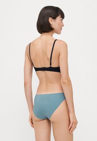 Black bikini top with adjustable straps and clasp closure; paired with a solid teal bikini bottom; smooth texture and minimal design.