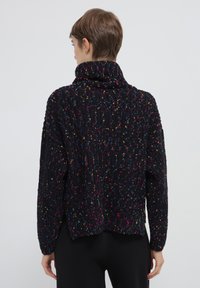 Maglione nero con colletto alto, superficie texturizzata, macchie colorate in rosa, blu, giallo e verde, vestibilità ampia con spalle basse.