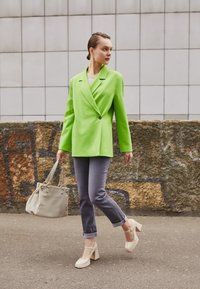 Ljusgrön strukturerad kavaj, grå jeans med uppvikt ärm, beige handväska och platåskor. Slät tyg och skräddarsydd passform med knapppdetalj.