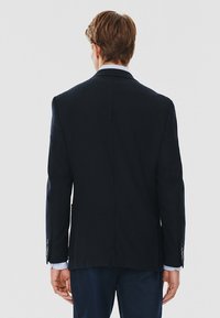 Granatowy blezer o dopasowanym kroju, z klapami w szpic i mankietami na guziki. Wykonany z teksturowanej tkaniny, charakteryzujący się czystym, prostym designem.