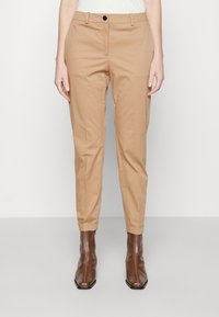 Beige nadrágok, szabott illeszkedéssel, egy gombos záródással és felhajtott szegőkkel, barna cipzáras bokacsizmával párosítva.