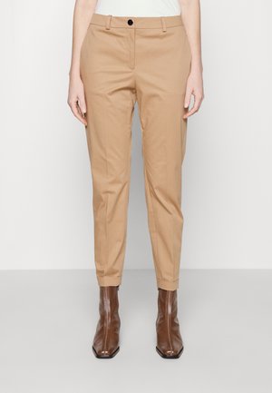 Pantaloni beige con vestibilità sartoriale, dotati di chiusura a singolo bottone e risvolti, abbinati a stivali alla caviglia marroni con zip.