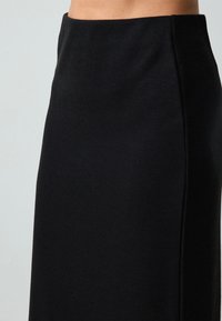 Jupe noire en tricot côtelé avec une taille haute, présentant une silhouette ajustée et une texture lisse. Pas de matériel ou de motifs visibles.