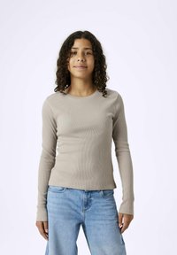 Langärmliges, ribbed Oberteil in hellbeige, mit Rundhalsausschnitt und taillierter Passform, kombiniert mit hellblauen, lässig geschnittenen Jeans.