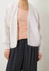 Vaaleanharmaa, pörröinen neuletakki pehmeästä materiaalista, avoin etuosa, pitkät hihat ja ribattu helma, käytetty vaaleanpunaisen kiinteän topin ja tummien housujen päällä.