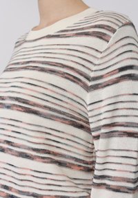 Gros plan sur une personne portant un pull en maille blanche avec des rayures horizontales noires et roses irrégulières.