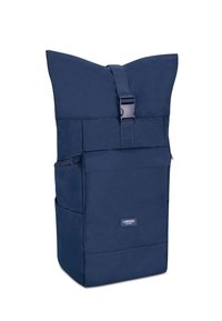 Sac à dos bleu marine avec un design à rabat, une sangle adjustable, une poche zippée à l'avant et une texture en tissu. Présente une étiquette de marque sur le devant.