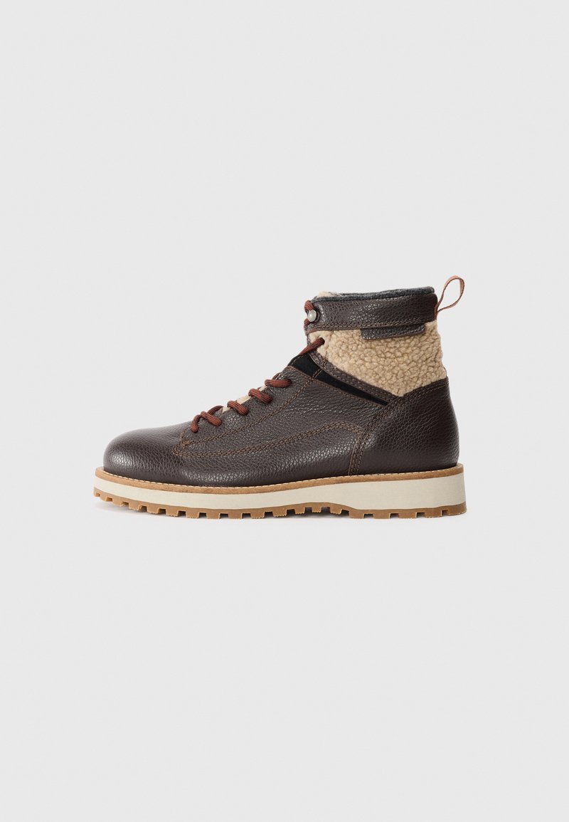 Brown leather boot with textured upper and beige fleece collar, featuring brown laces, light-colored sole, and rugged tread.