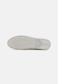 Suola di sneaker bianca con materiale in gomma, grip texturizzato e logo circolare; bordi lisci e motivo di battistrada minimale.