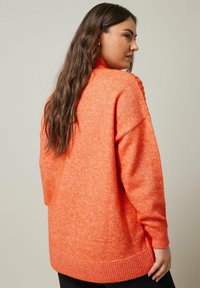 Überdimensionaler oranger Strickpullover mit strukturiertem Finish, gerippten Bündchen und hohem Kragen. Entworfen für Komfort und Wärme.
