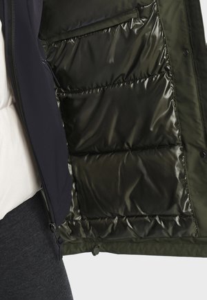 Giubbotto imbottito verde scuro con una fodera interna lucida, dotato di chiusura a zip e tasche laterali. L'esterno è strutturato e morbido.