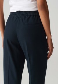 Pantalons bleu marine en tissu texturé, avec une ceinture élastique et une poche arrière. Fini lisse et coupe droite.
