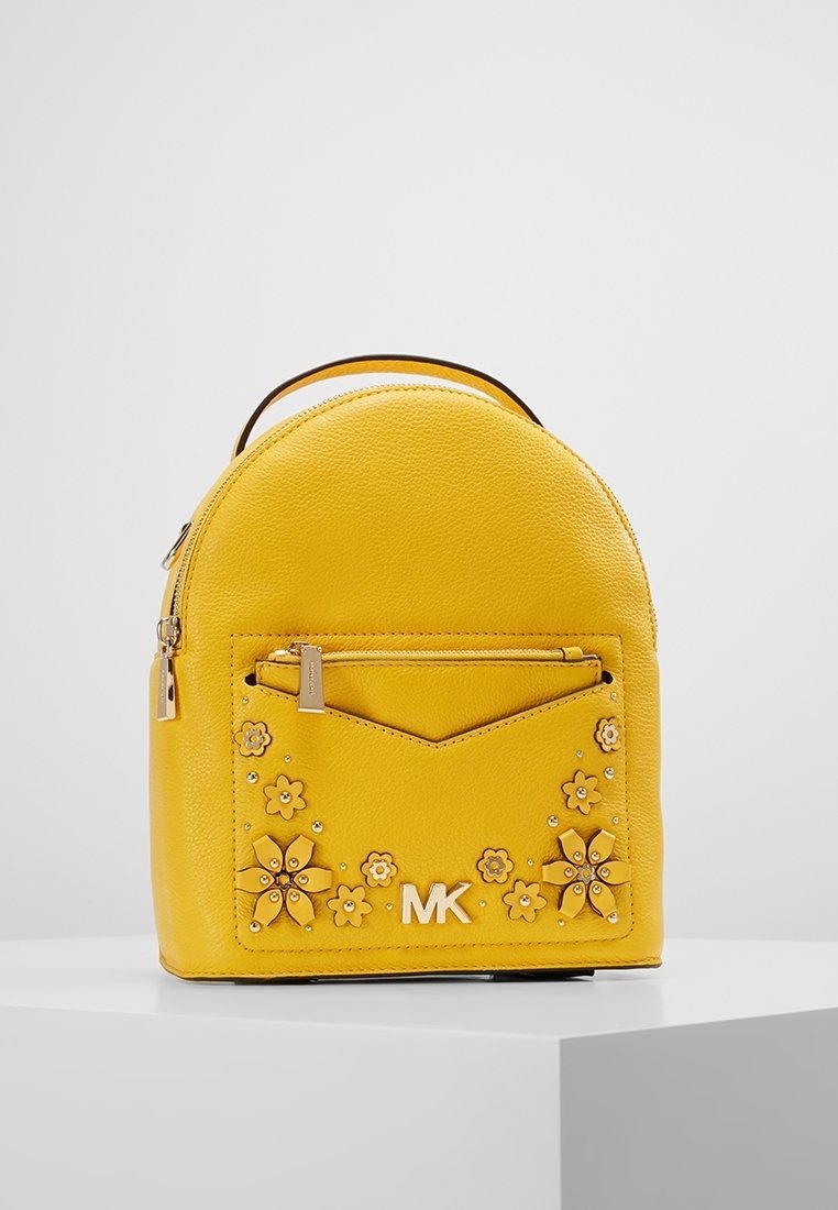 Mochila de cuero amarilla con parte superior redondeada, bolsillo frontal, adornos florales y herrajes en tono dorado. Presenta un logotipo prominente en la parte frontal.