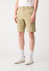 Beige cargo shorts made of cotton with side pockets, a button closure, and a tailored fit, paired with white sneakers and crew socks.