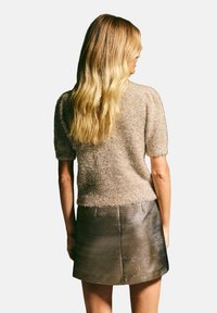 Gebreide trui met korte mouwen in lichtgoud met een zachte textuur, gecombineerd met een metallic, geribbelde mini-jurk met horizontale strepen.