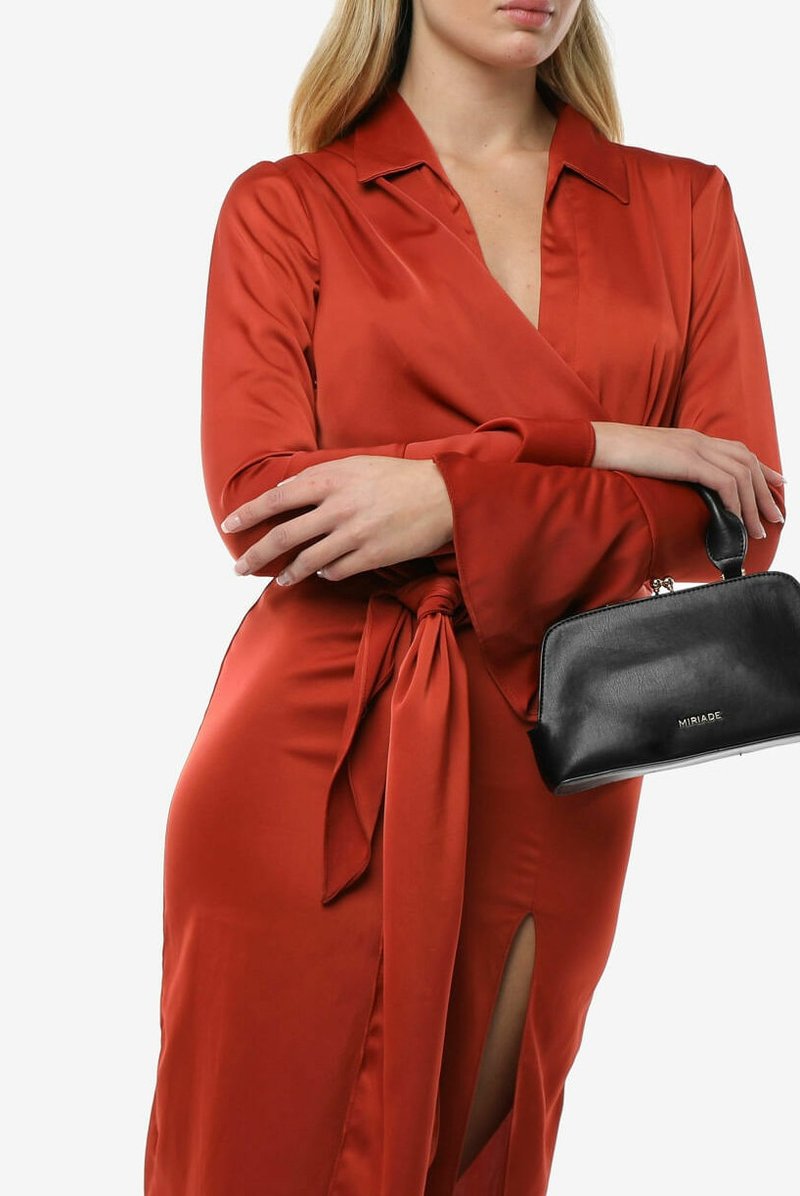 Abito avvolgente in raso rosso con vita regolabile, maniche lunghe e uno spacco laterale. Abbinato a una piccola borsa a tracolla in pelle nera.