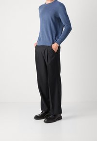 Niebieski sweter dzianinowy z długimi rękawami, zestawiony z czarnymi spódnicami plisowanymi i czarnymi butami. Sweter ma małe logo.