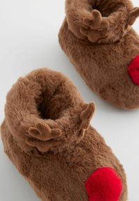 Bruna fluffiga tofflor med rullad mudd, små horndetaljer och en röd pom-pom näsa. Mjuk textur och kompakta former.