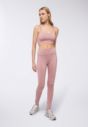 Completo sportivo rosa composto da un reggiseno aderente con spalline sottili e leggings a vita alta. Il materiale è liscio con una leggera lucentezza.
