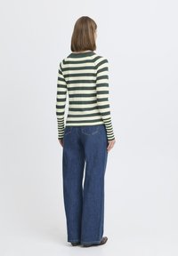 Top de manga larga a rayas en verde y crema, combinado con unos jeans de pierna ancha de cintura alta en azul oscuro, visto desde atrás, mostrando las mangas y el ajuste.