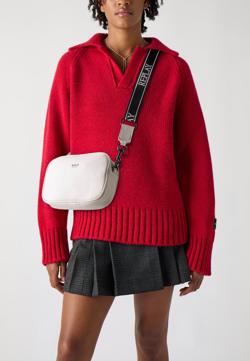 Roter Strickpullover mit Kragen, versehen mit gerippten Bündchen und Saum. Schwarzer und grauer Karo-gefälteter Rock. Weiße rechteckige Handtasche mit verstellbarem Riemen.
