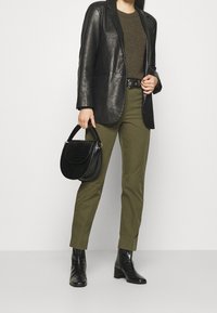 Zwarte leren blazer, olijfgroene broek en zwarte croco-embossed handtas. Zwarte haklaarzen met een gestructureerde afwerking. Eenvoudig, klassiek ontwerp.