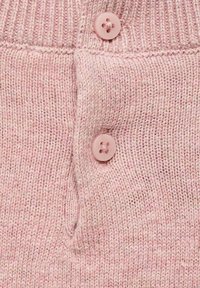 Měkká růžová pletenina s dvěma odpovídajícími kulatými knoflíky přišitými na vroubkovaném, texturovaném povrchu.