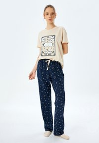 Beige Baumwoll-T-Shirt mit Wolkenmotiv und dem Text "DAS NICKERN." Marineblaue Schlafanzughose mit einem Muster aus Sternen und Planeten. Weicher Stoff, lockere Passform.