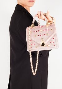 Rosa sammetshandväska med guldkedja, prydd med färgglada stenar och intrikata detaljer, med en låsdekoration på framsidan.