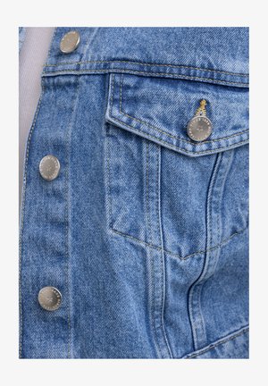 Svijetloplavi traper jakna sa srebrnim dugmadi, džepom na prsima i kontrastnim šavovima. Materijal ima teksturiranu završnu obradu s klasičnim dizajnom.