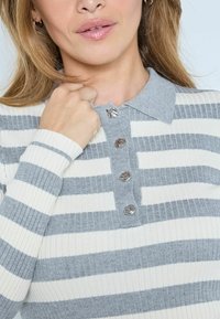 Csíkos bordázott pulóver szürke gallérral, négysoros gombolattal és felváltva szürke és fehér vízszintes csíkokkal.