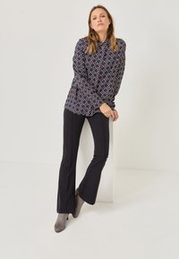 Marinebluse med et geometrisk mønster, parret med sorte flarebukser. Outfittet er suppleret af grå hæletter.