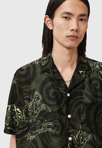 Short-sleeve black shirt with green dragon and swirl patterns, made of lightweight fabric; features a classic collar and button closure.