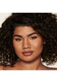 Portrait of a person with curly, dark hair, warm skin tone, defined eyebrows, and full lips, showcasing a natural makeup look.