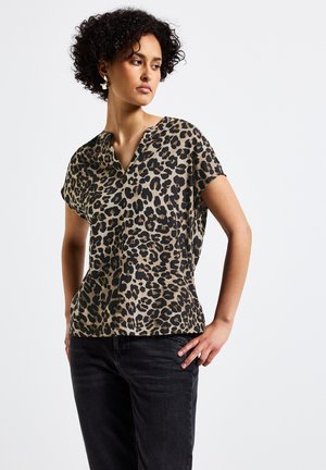 Blusa con stampa leopardata in beige e nero, maniche corte, scollatura a V, tessuto leggero, indossata con jeans scuri. Presenta una vestibilità rilassata.