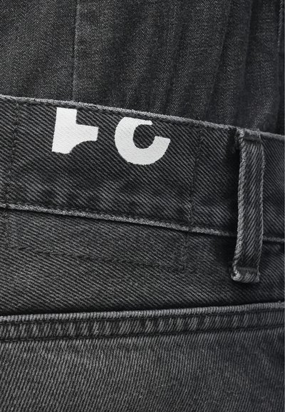 Černé džíny z denim s texturovaným povrchem. Obsahují bílé logo na pásku a šedé švy. Zahrnují detail s poutky na opasek.