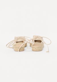 Beige Espadrilles mit Juteböden und Obermaterial aus Stoff, ausgestattet mit langen Schnürsenkeln, die hinten gebunden sind, und offenen Seiten.