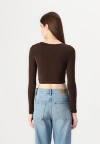 Brun cropped langermet topp med glatt tekstur. Kombinert med lyseblå høyt midjejeans med logopatch og baklommer.
