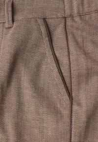Tissu marron texturé avec un motif en chevrons, comportant une poche avant soulignée d'une bordure marron plus foncé et une taille lisse.