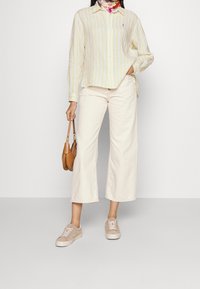 Light yellow and white striped long-sleeve shirt, cream wide-leg pants, beige sneakers, and a brown handbag, styled with a colorful scarf.