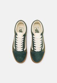 Gröna mockaskor med vita snören, med en beige sidreifen och en sula av gummigummi. Rund tå och texturerad ovandel.