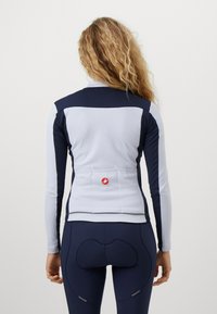 Långärmad cykeltröja i ljusgrått med marinblå accenter; har texturerade paneler, en zipkrage och en logopatch på ryggen.