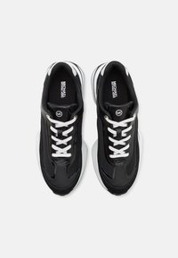 Črne superge z mešanico usnja in mrežastih materialov, z belimi vezalkami, oblazinjeno podplatom in elegantnim dizajnom.