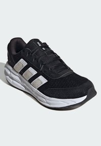 Czarne buty sportowe z białymi akcentami, siateczkowa cholewka, teksturowane materiały, wyściełany kołnierz oraz gumowa podeszwa zaprojektowana dla komfortu i wsparcia.